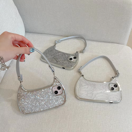 A hand holding one of three silver glittery purse-style phone cases resting on a light-colored couch.