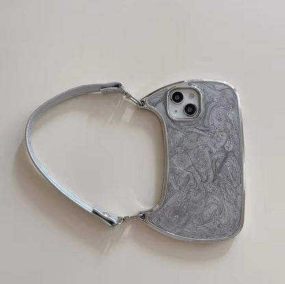 Introducing the Curved Cases Electroplated Handbag Hand Strap Phone Case for iPhone models 15 through 7, including Pro and Max versions. This unique case is designed to resemble a small handbag and features a stunning marble-like pattern in shades of gray, adorned with glittering metallic waves. The short strap attached to the corners makes it easy to carry, while the silver-colored edges perfectly complement its sophisticated design.